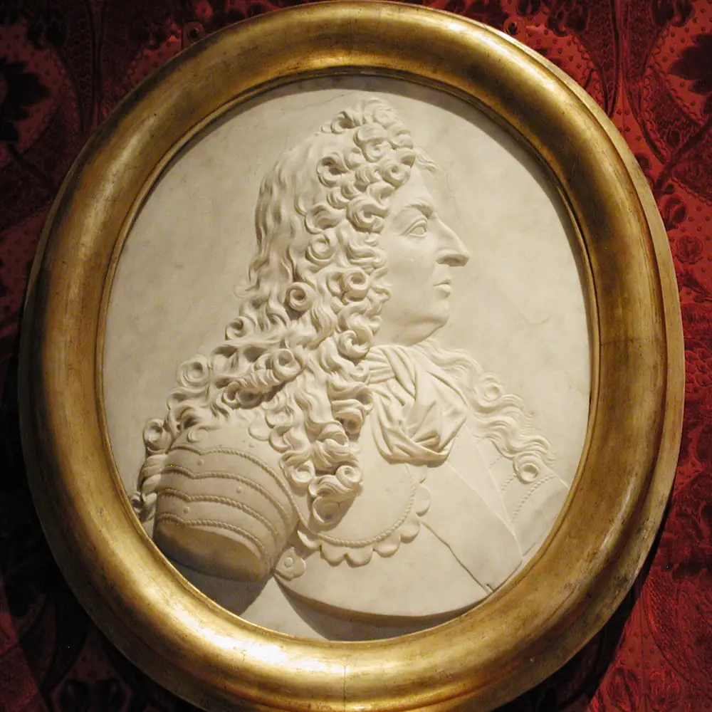Photographie d’un portrait de Louis XIV en relief de marbre, dans son cadre ovale doré, fin du XVIIᵉ siècle : une pièce dont le transport, la restauration et l’encadrement laissent chacun une facture à rattacher.