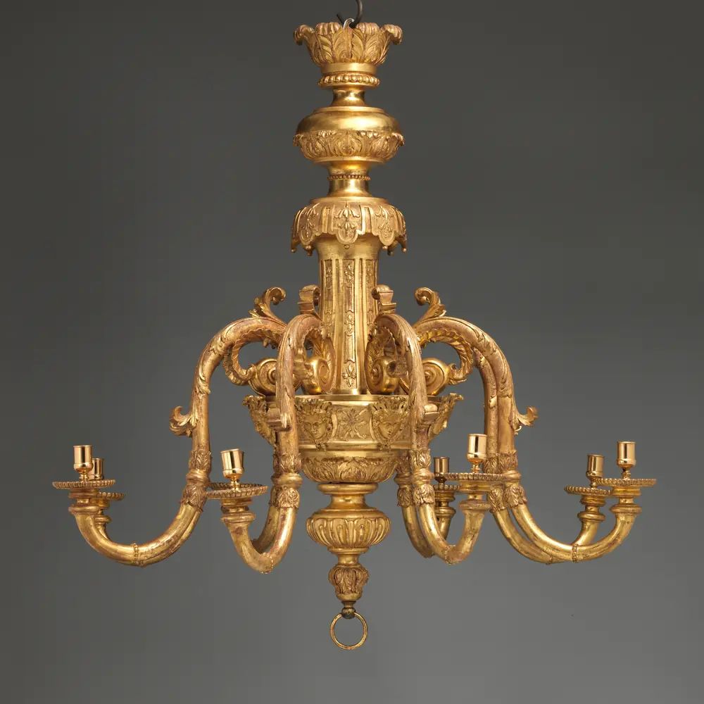 Photographie d’un lustre à huit bras en bois doré et gesso, vers 1710, suspendu sur fond gris : une pièce qu’un client peut vous redemander des mois après l’avoir vue.