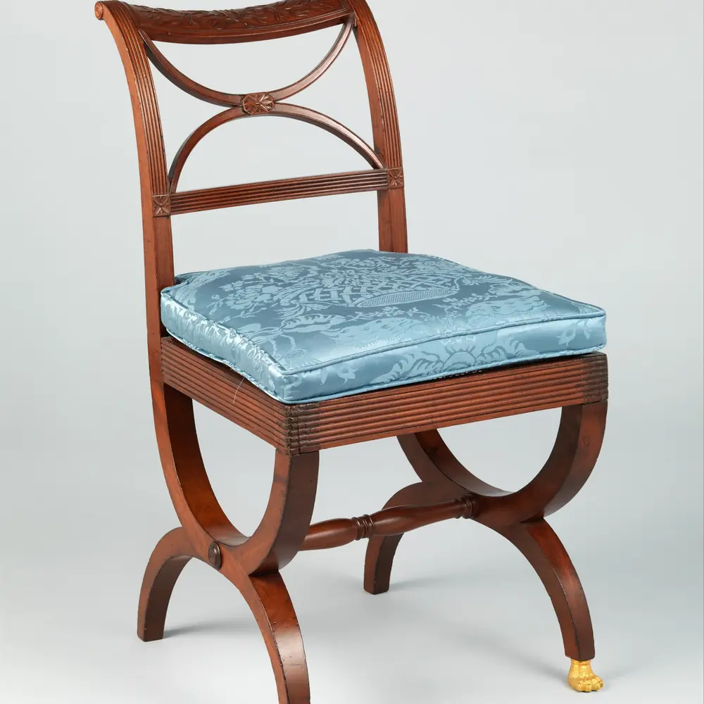 Photographie d’une chaise en acajou à dossier ajouré et pieds en X terminés par une patte dorée, début du XIXᵉ siècle : le genre de pièce repérée sur place, et gardée pour plus tard.
